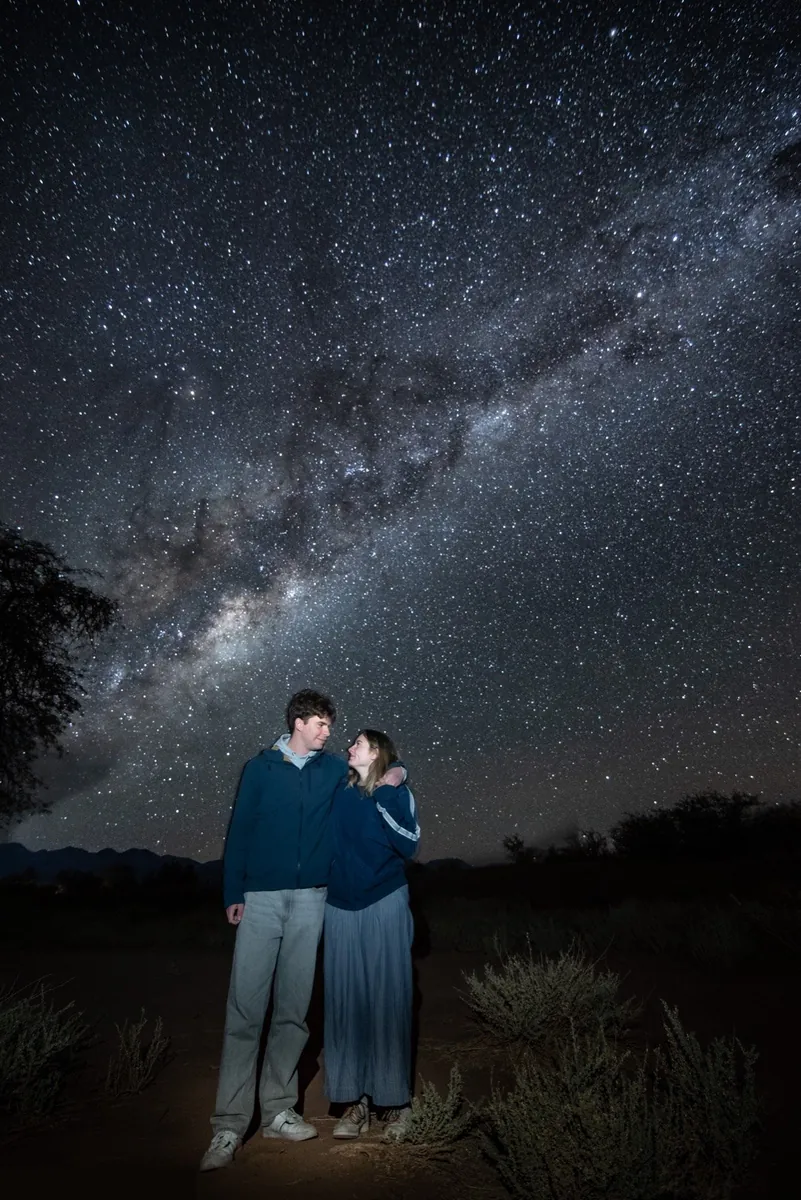 Pareja iluminada mirándose mutuamente con la Vía Láctea de fondo