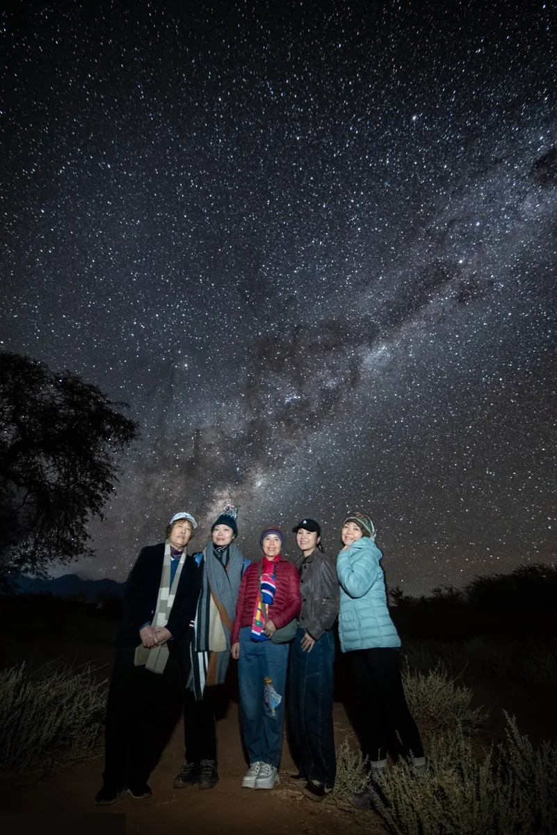 Grupo de 5 mujeres iluminadas posando bajo la Vía Láctea en Atacama