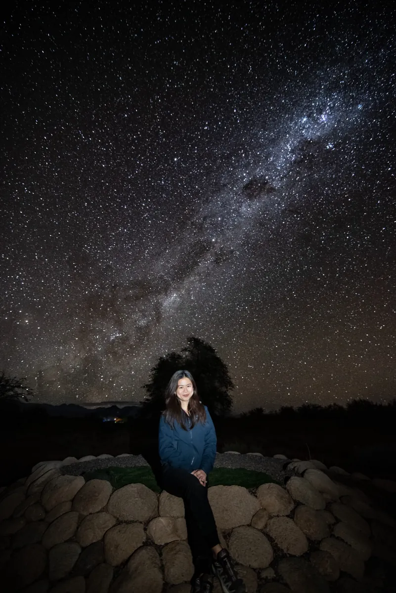 Mujer sola con chaqueta azul iluminada bajo la Vía Láctea en el desierto de Atacama