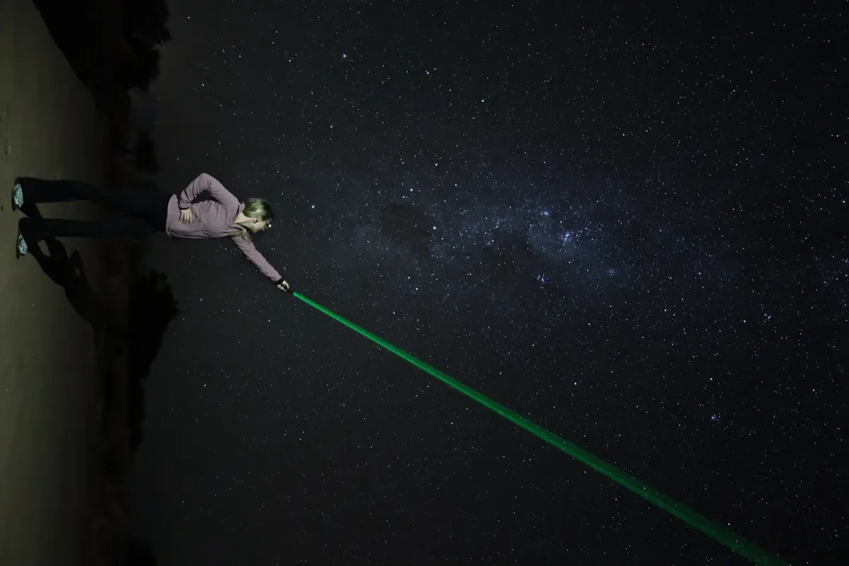 Mujer señalando el cielo con puntero láser verde durante la charla astronómica nocturna