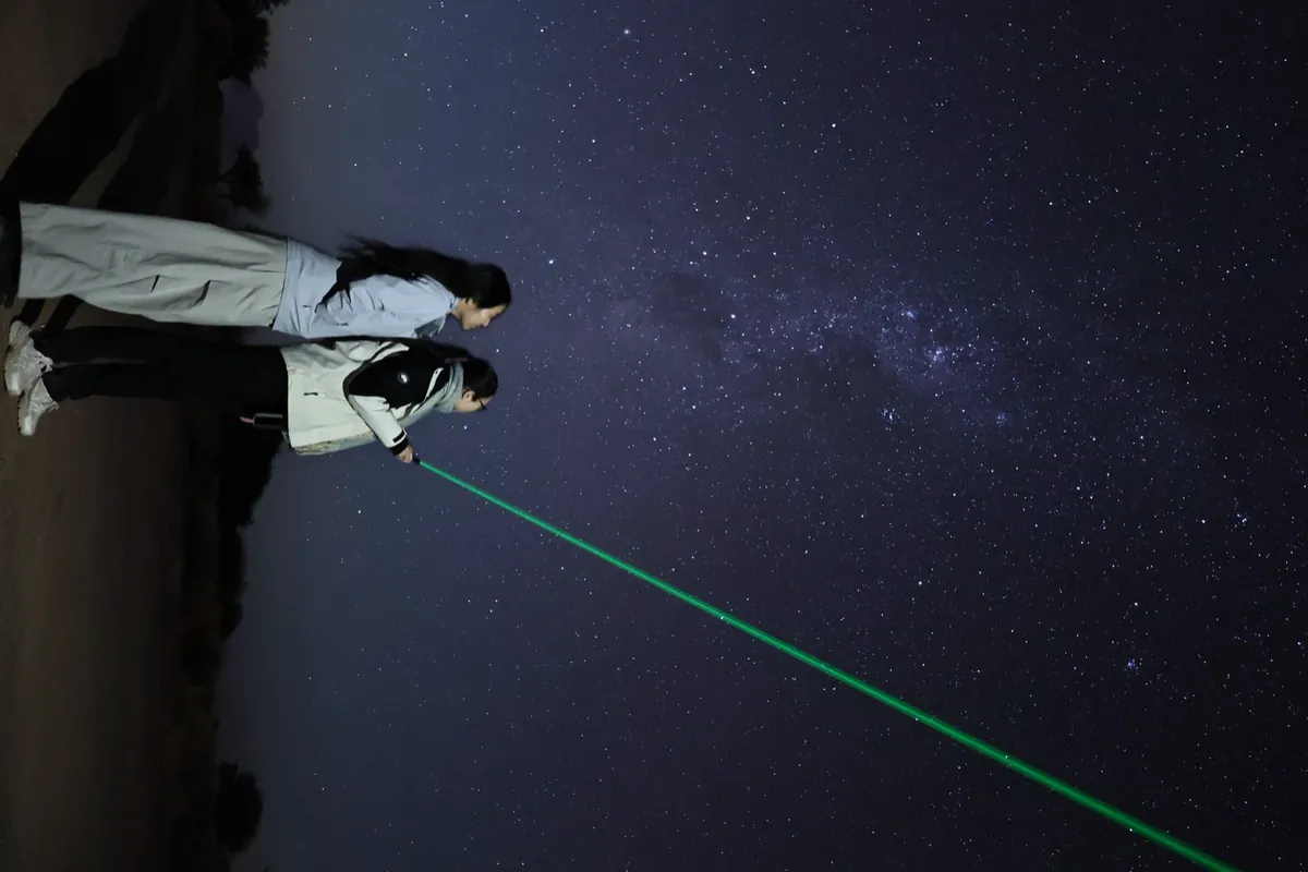 Dos mujeres señalando el cielo con puntero láser verde durante la charla nocturna