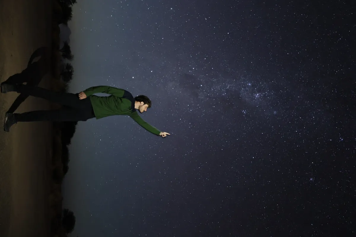 Hombre señalando constelaciones bajo un cielo azul y violeta intenso con puntero láser