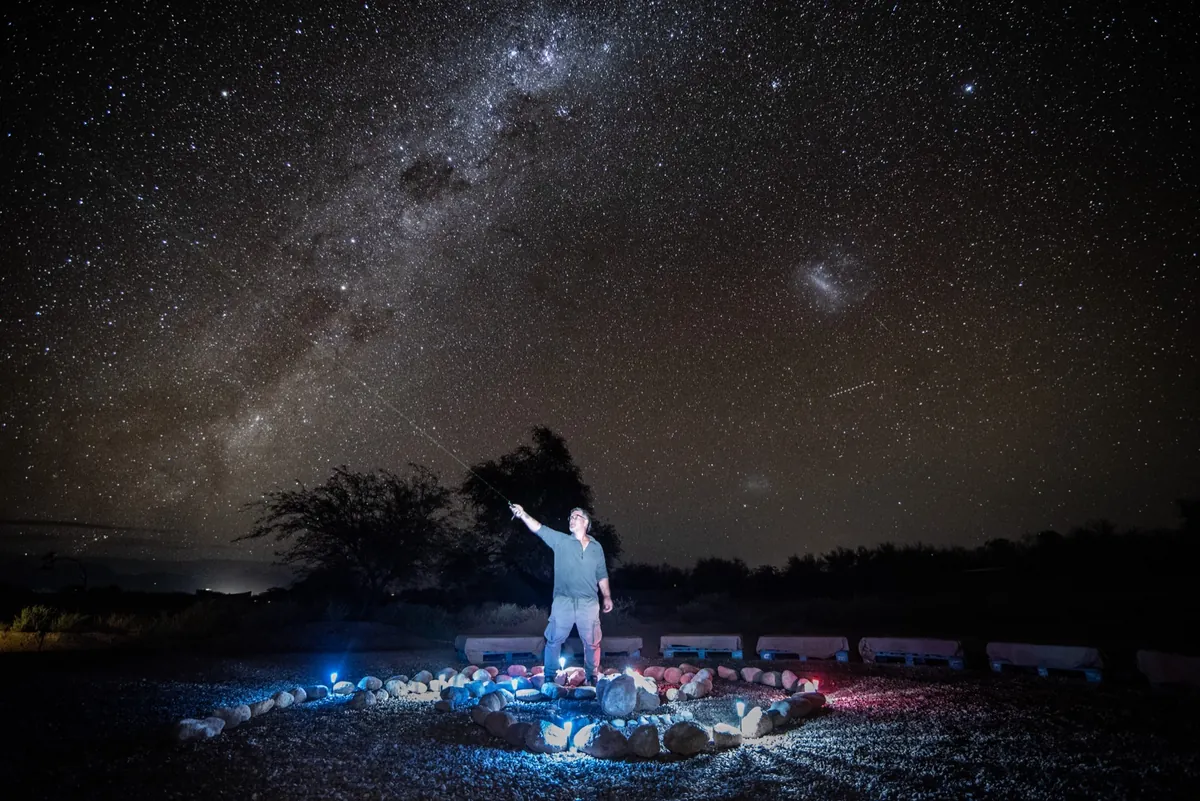 Guía señalando el cielo con puntero láser verde, rodeado del círculo de piedras iluminado durante la charla astronómica