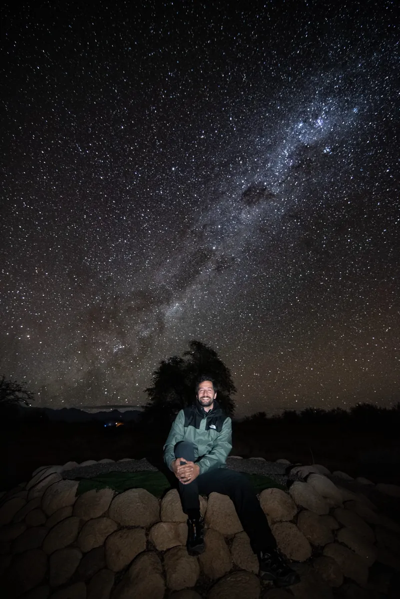 Hombre sonriendo iluminado bajo la Vía Láctea en el desierto de Atacama