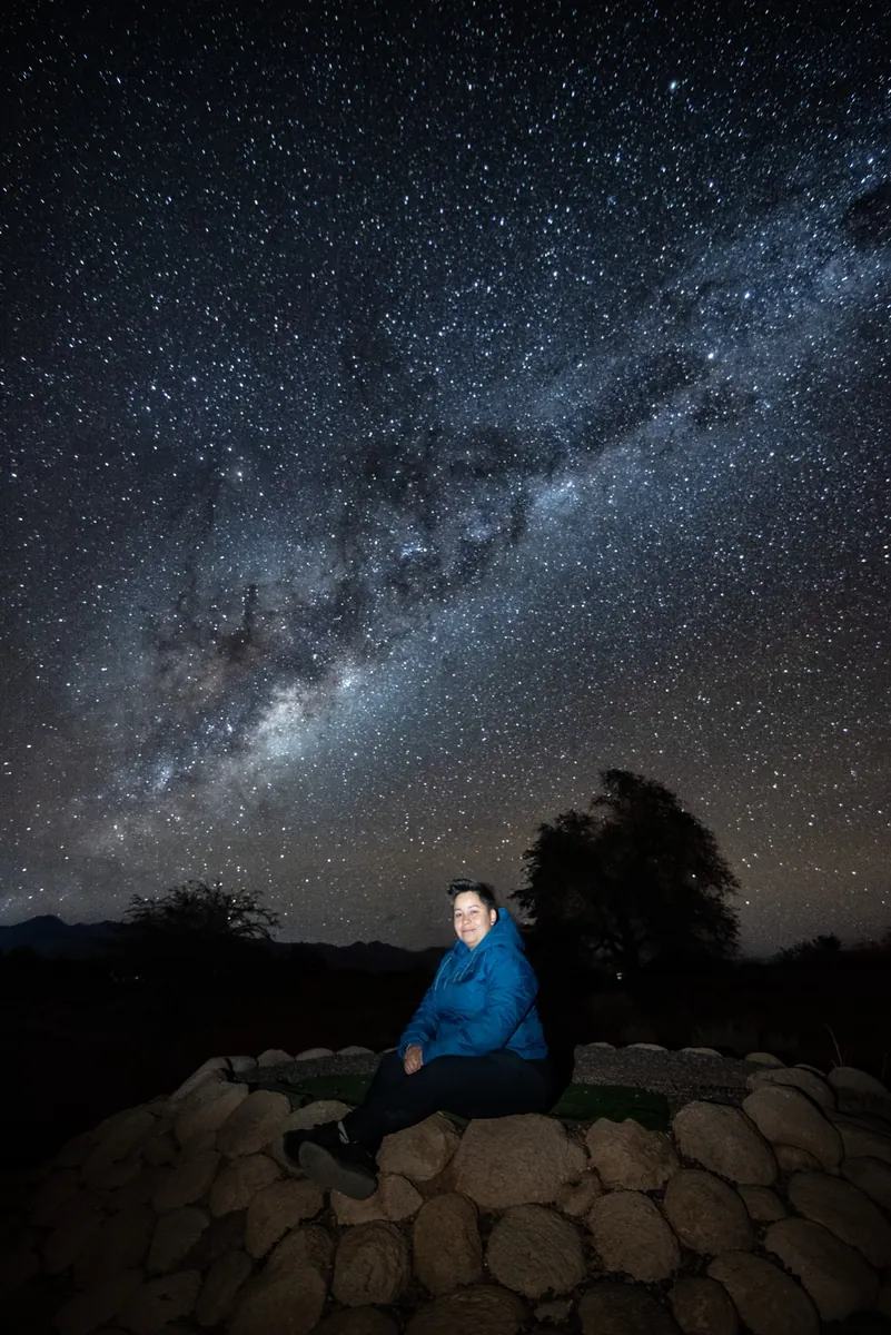 Mujer con chaqueta azul iluminada bajo una Vía Láctea espectacular en Atacama
