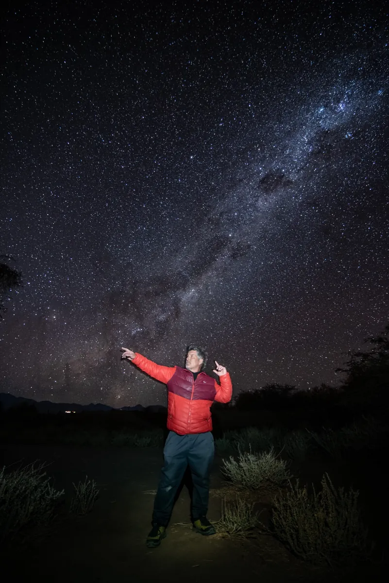 Ignacio con chaqueta roja señalando el cielo nocturno en el desierto de Atacama