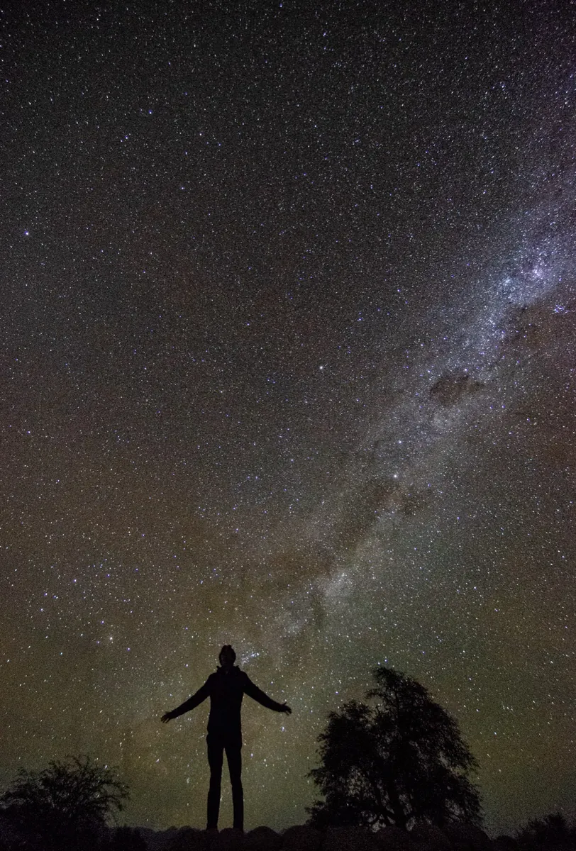 Silueta de hombre con brazos abiertos contemplando la Vía Láctea en Atacama
