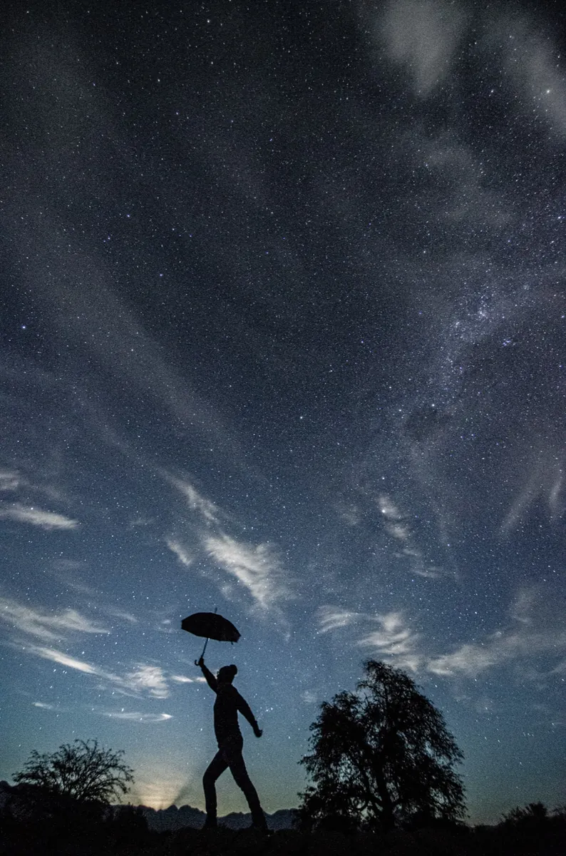 Silueta de Jaime con paraguas bajo la Vía Láctea y nubes en cielo azul profundo